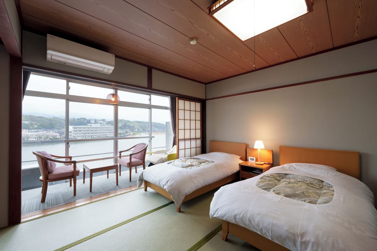 Een hotelkamer met twee bedden, uitzicht op een rivier en een traditioneel Japans interieur.