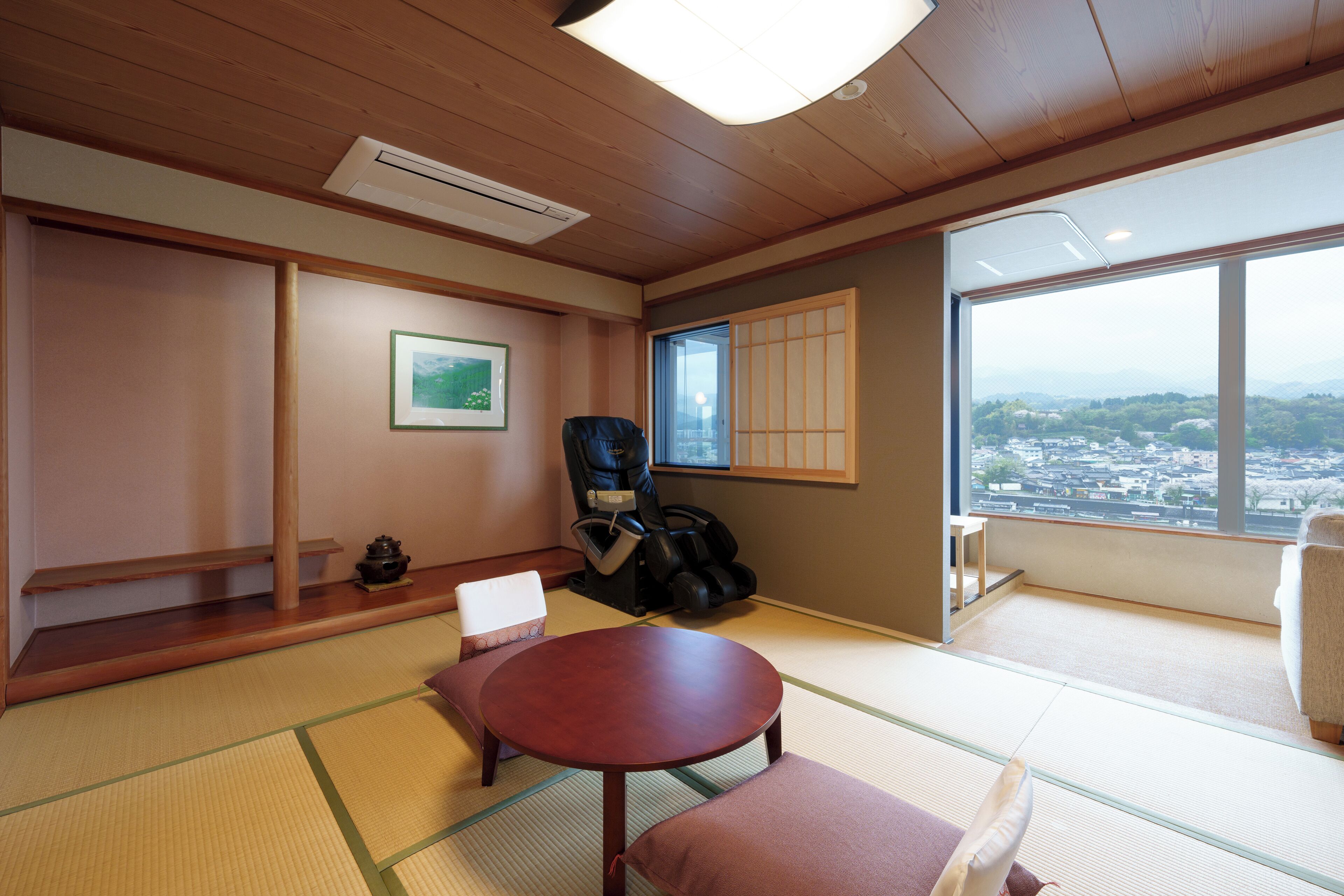 A traditional Japanese room with tatami flooring, a low table, a cushioned bench, a black chair, and a view of a cityscape through a large window.