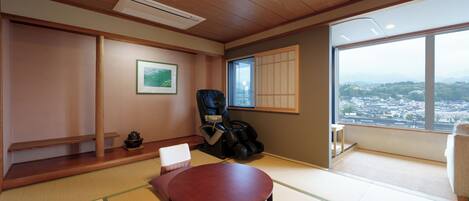 A traditional Japanese room with tatami flooring, a low table, a cushioned bench, a black chair, and a view of a cityscape through a large window.