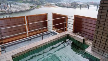 Vista desde un balcón sobre un río con un puente, un edificio y montañas al fondo.