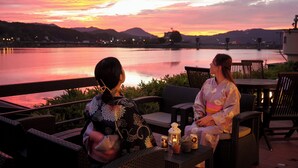 Two people seated at an outdoor table with a view of a lake and mountains during sunset.
