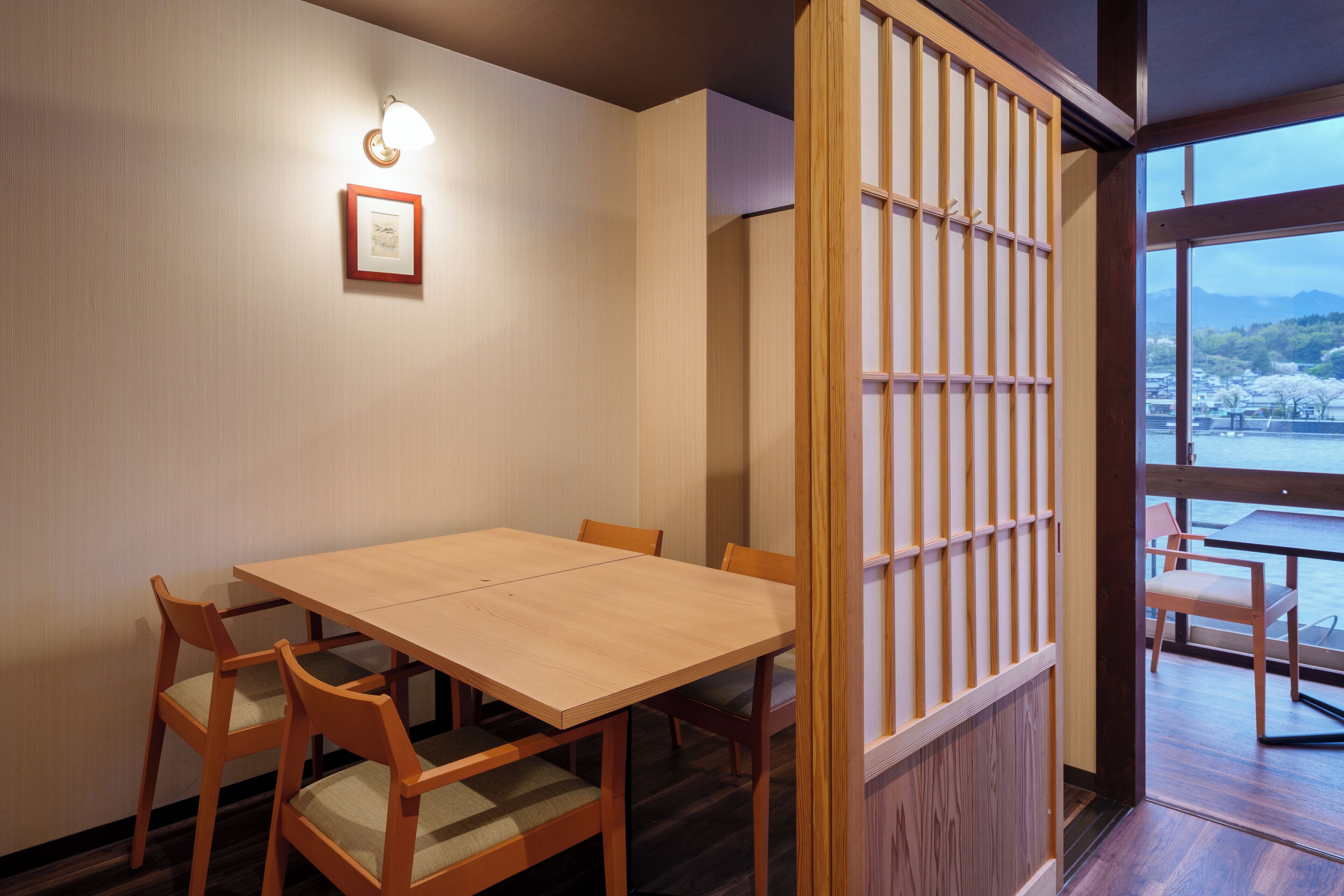 A traditional Japanese-style room with a wooden table and chairs, a shoji screen, and a view of cherry blossoms.