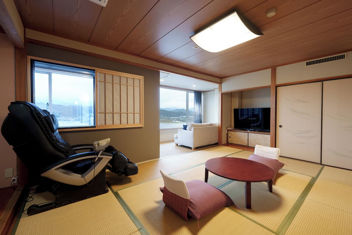 Een kamer met tatami vloerbedekking, een massagestoel, een televisie en een bank.