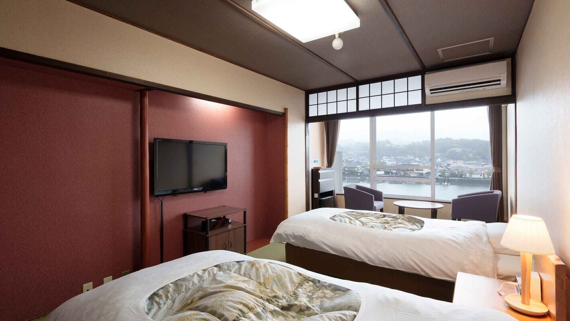 A hotel room with two beds, a TV, a desk, and a large window with a view of a cityscape.