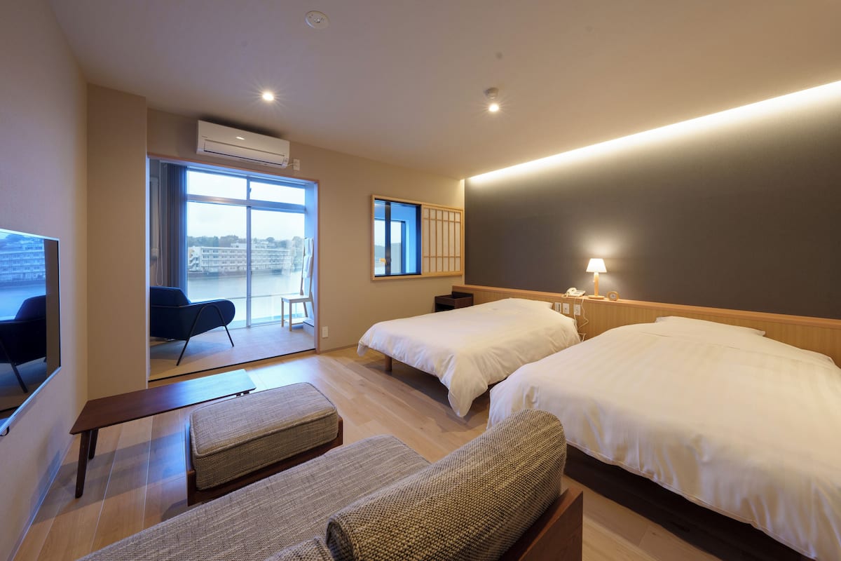 Hotelkamer met twee bedden, een bankje, een stoel en een groot raam met uitzicht.