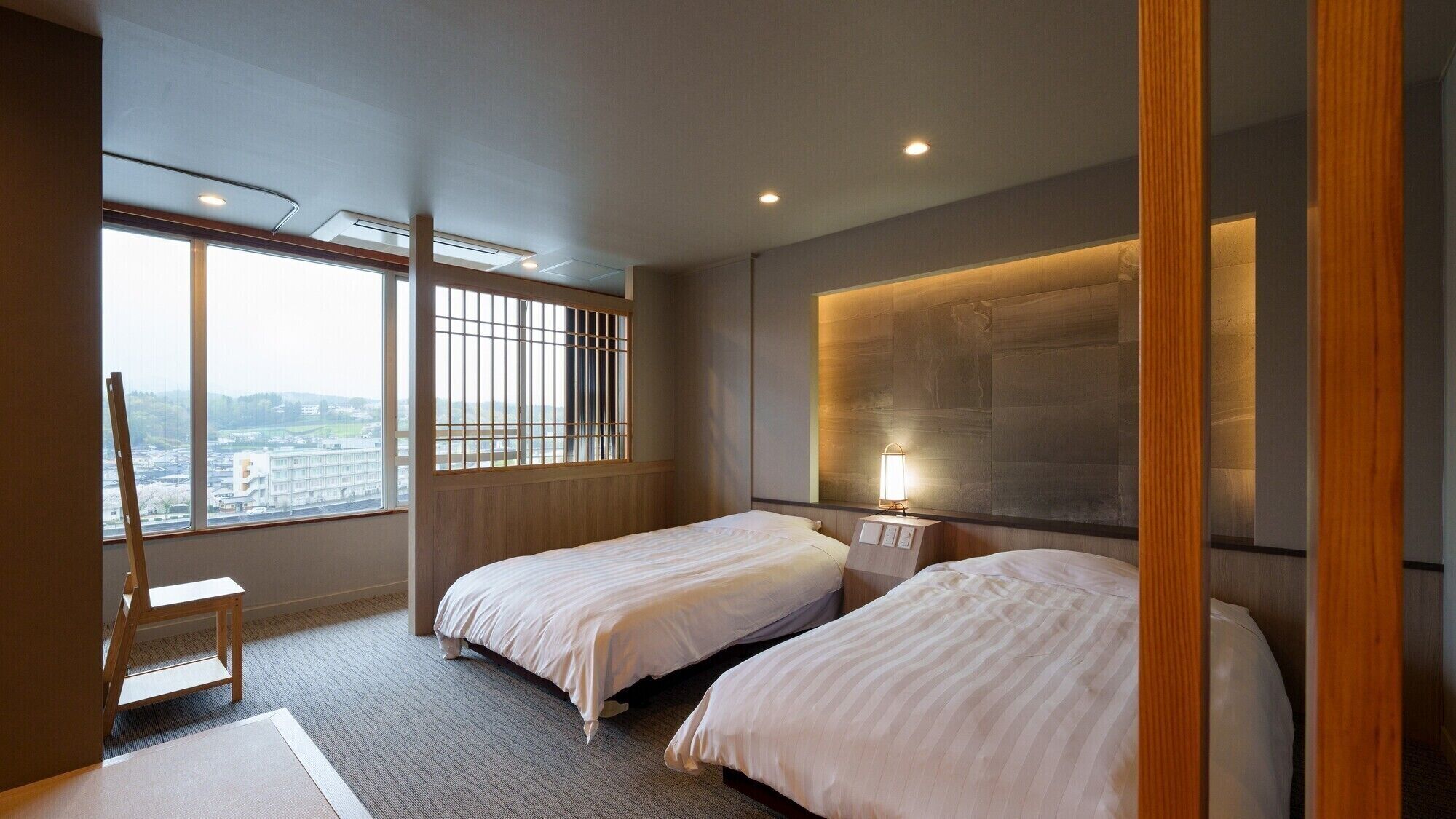 Ein Hotelzimmer mit zwei Betten, einem großen Fenster mit Aussicht, einer Stehlampe und einem Holzstuhl.