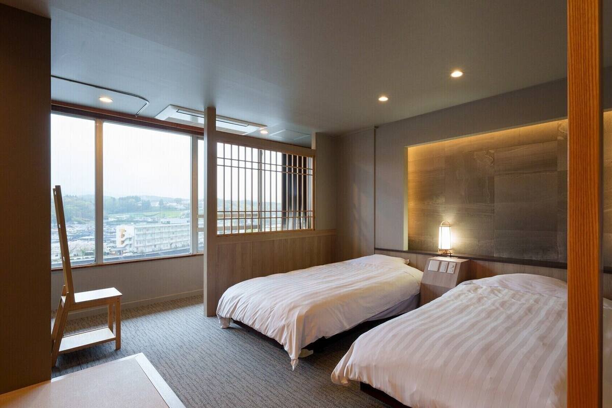 Een hotelkamer met twee bedden, een groot raam met uitzicht, een staande lamp en een houten stoel.
