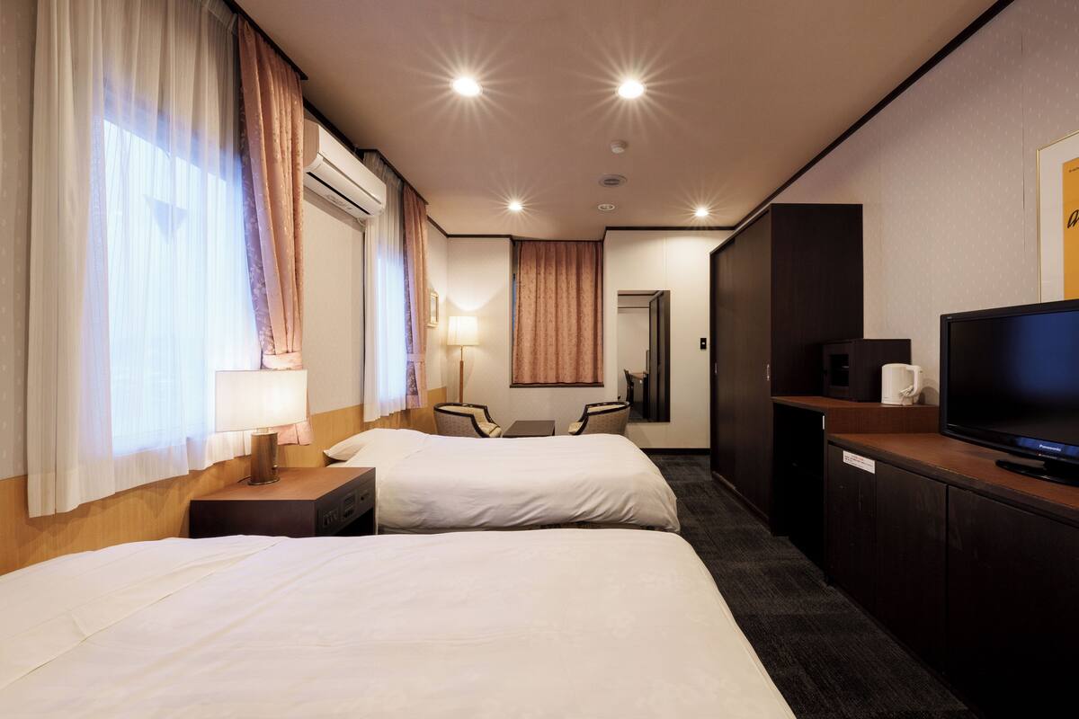 Een hotelkamer met twee bedden, een bureau met een lamp, een televisie en een badkamer op de achtergrond.