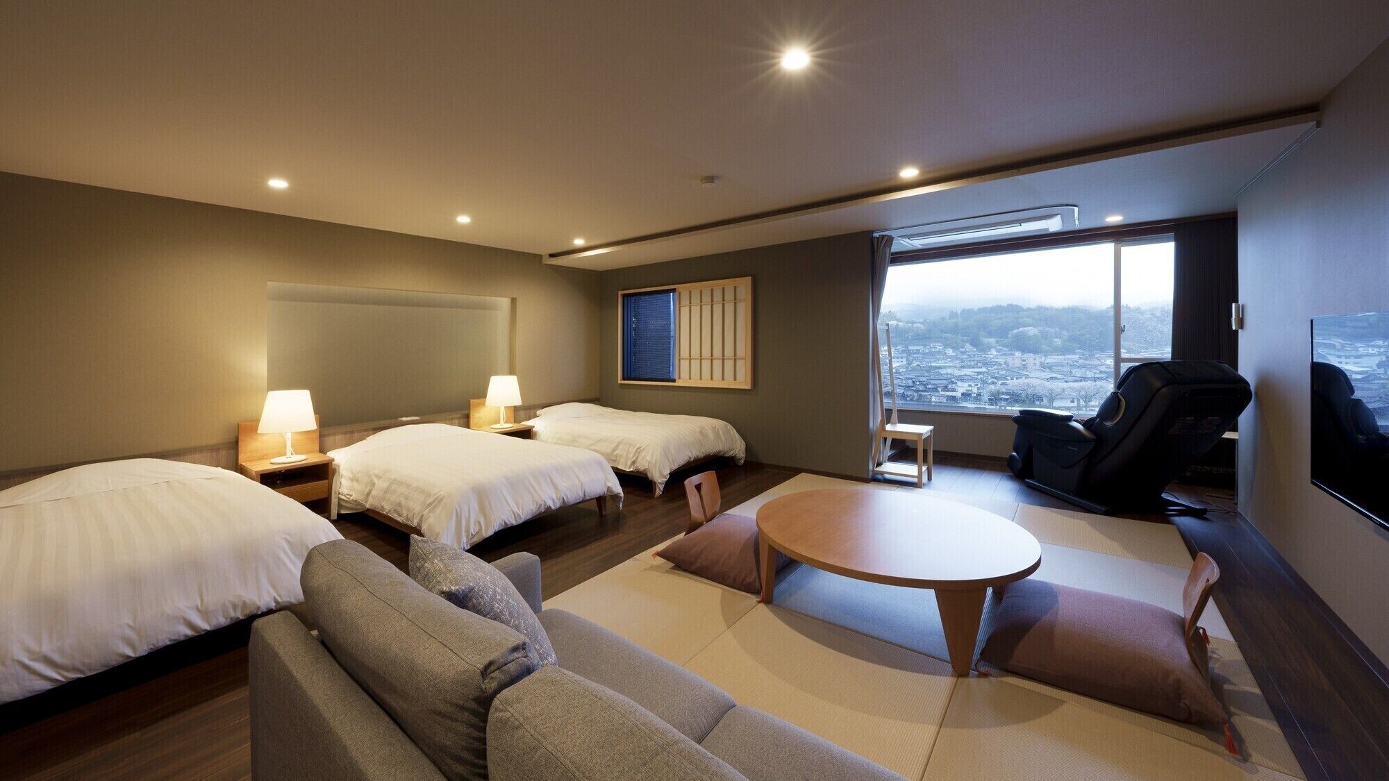 Ein Hotelzimmer mit zwei Betten, einem Schlafsofa, einem kleinen Tisch und Blick auf eine Stadtlandschaft.