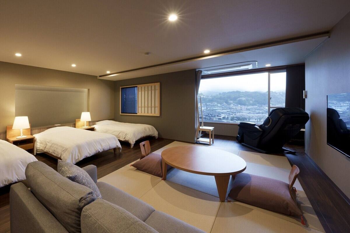 Een hotelkamer met twee bedden, een bank, een eettafeltje en uitzicht op een stadsgezicht.