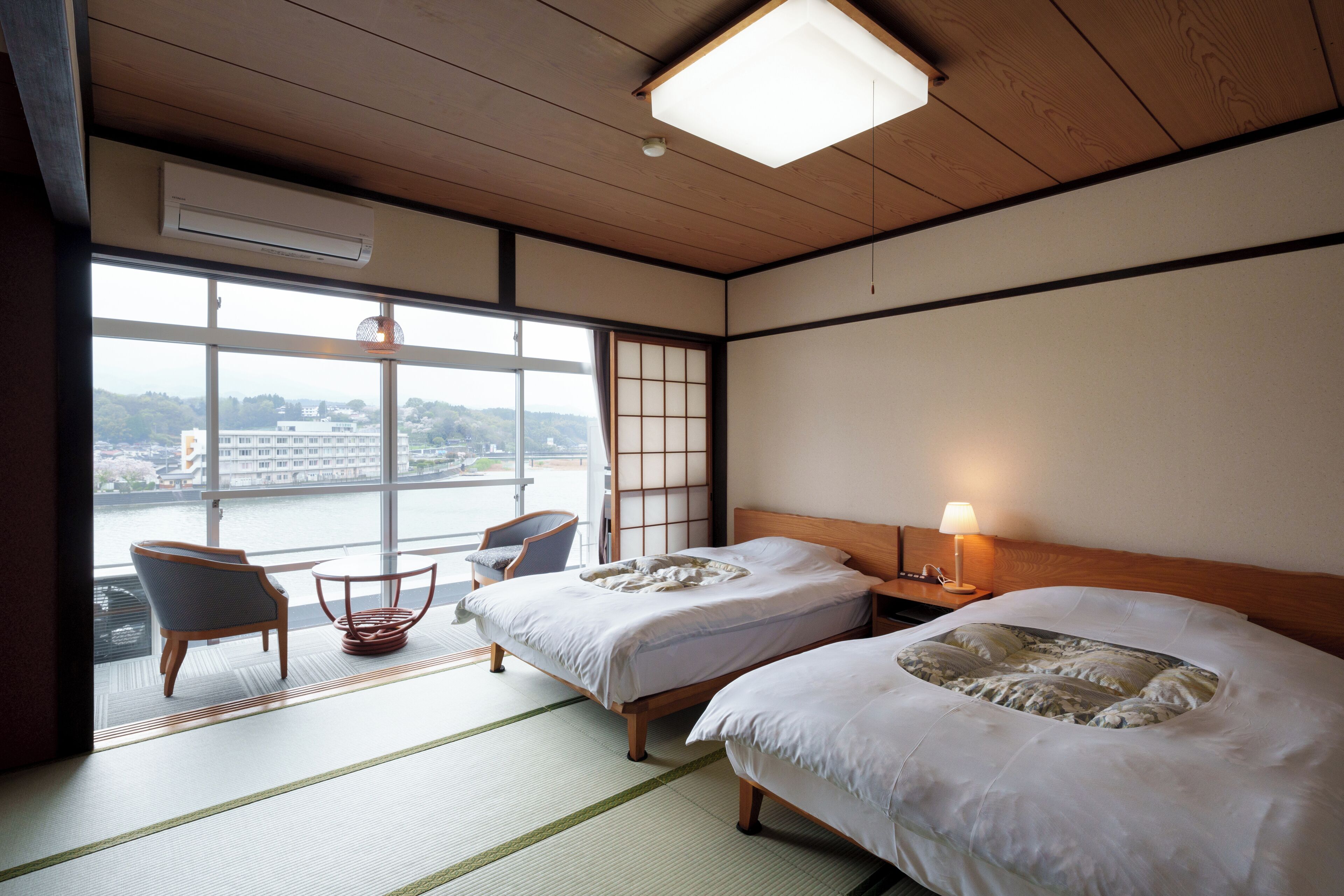A hotel room with two beds, a view of a river, a chair, and a table.