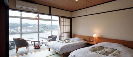 A hotel room with two beds, a view of a river, a chair, and a table.