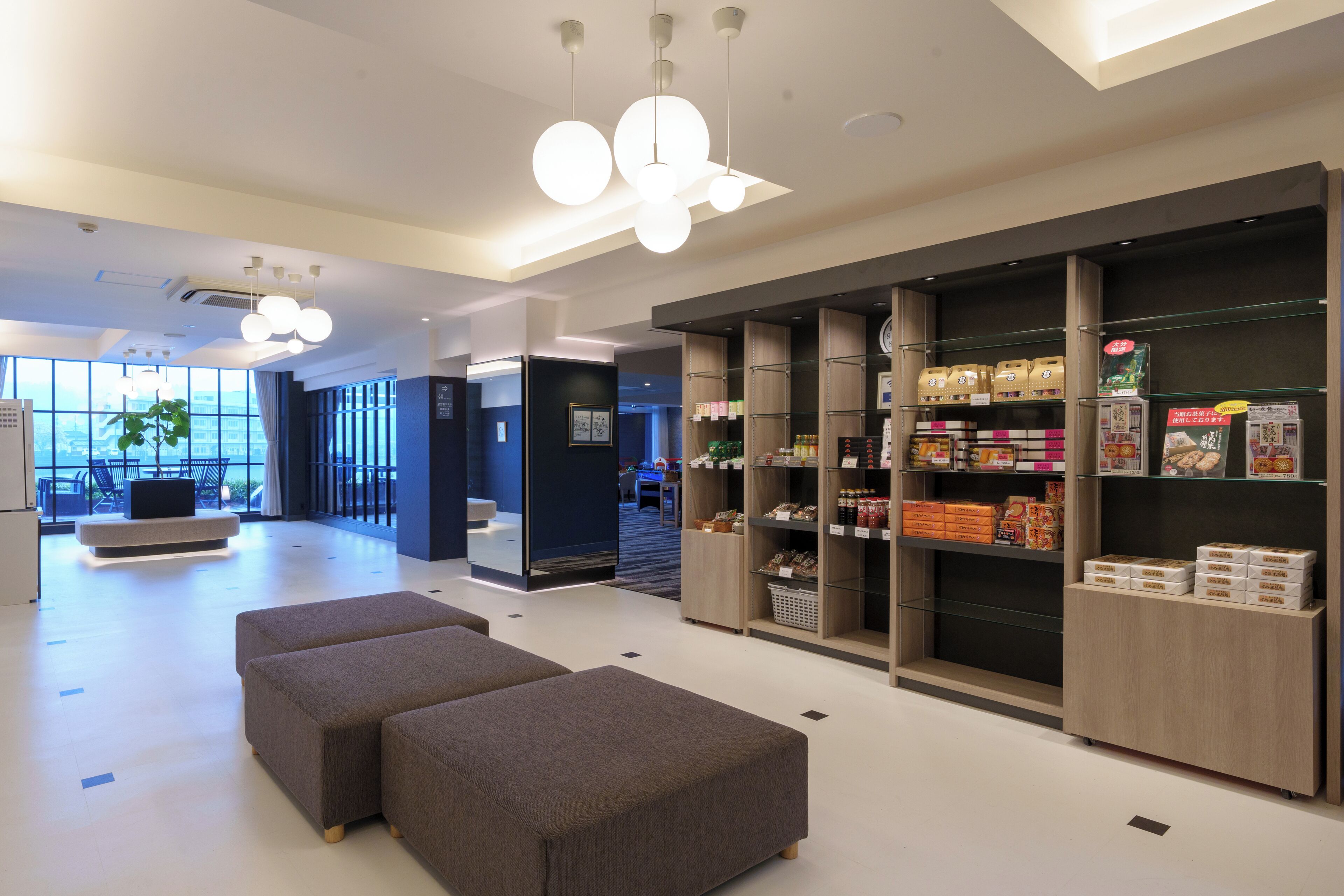Un moderno vestíbulo de hotel con áreas de descanso, un mostrador de recepción y diversas comodidades, como una estación de café y un bar de aperitivos.