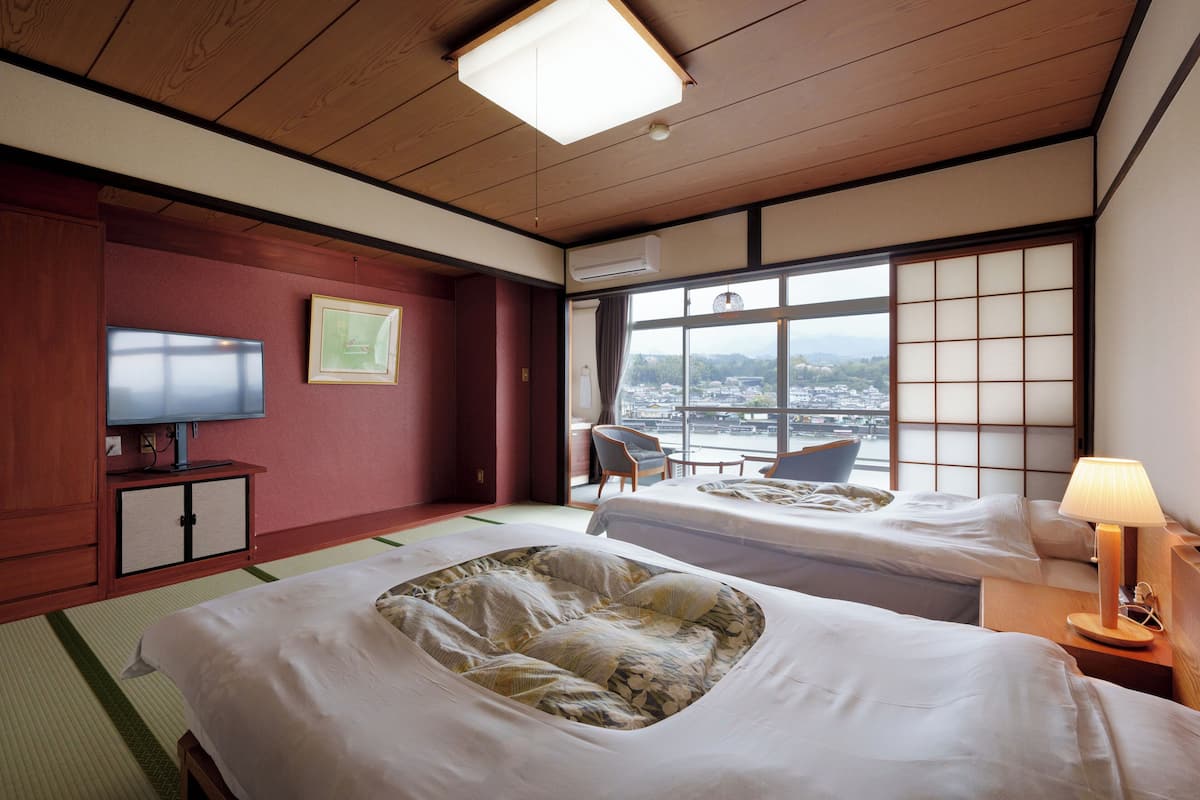 Een hotelkamer met twee bedden, een televisie, een stoel en uitzicht op de stad door grote ramen.