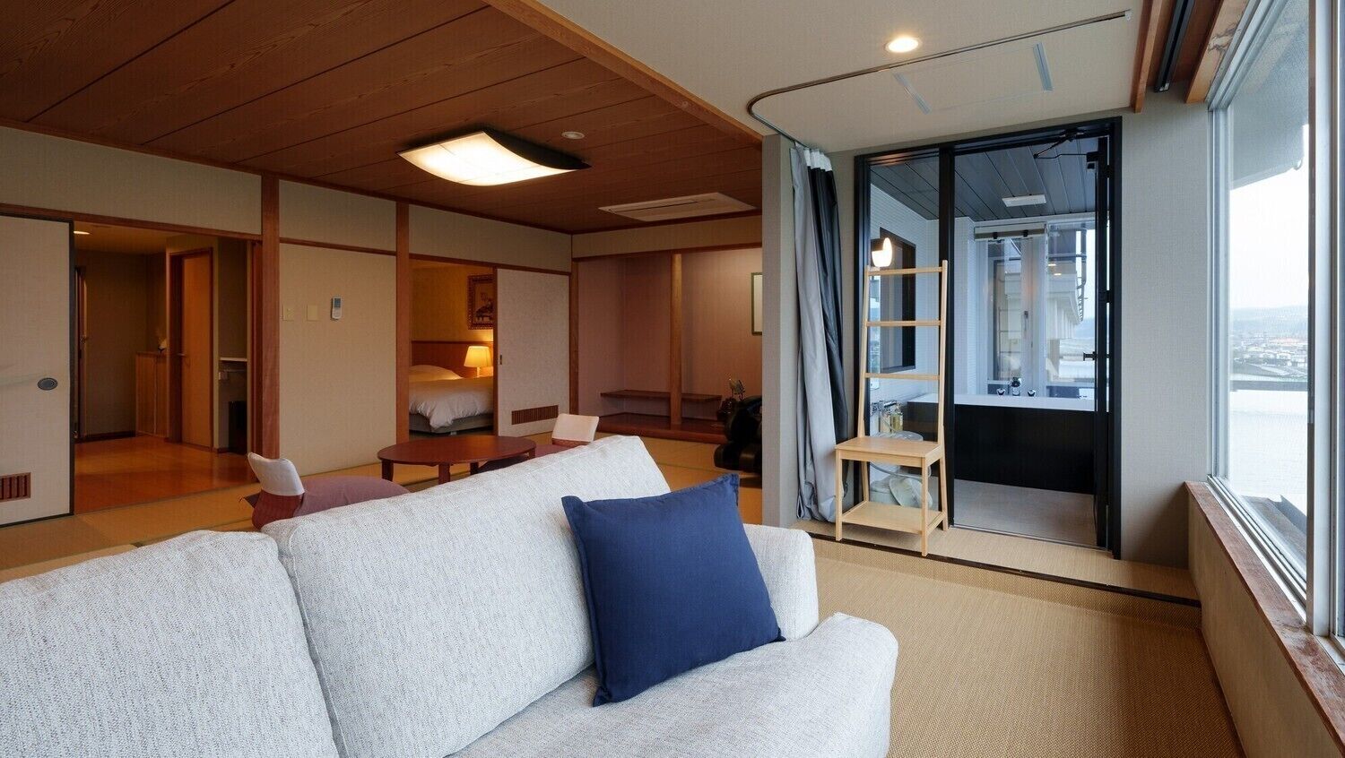 Ein modernes Hotelzimmer mit einer Couch, einem Essbereich und einer Küche, die durch eine Schiebetür sichtbar ist.