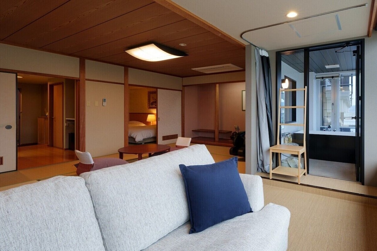 Een moderne hotelkamer met een bank, een eethoek en een keuken, zichtbaar door een schuifdeur.