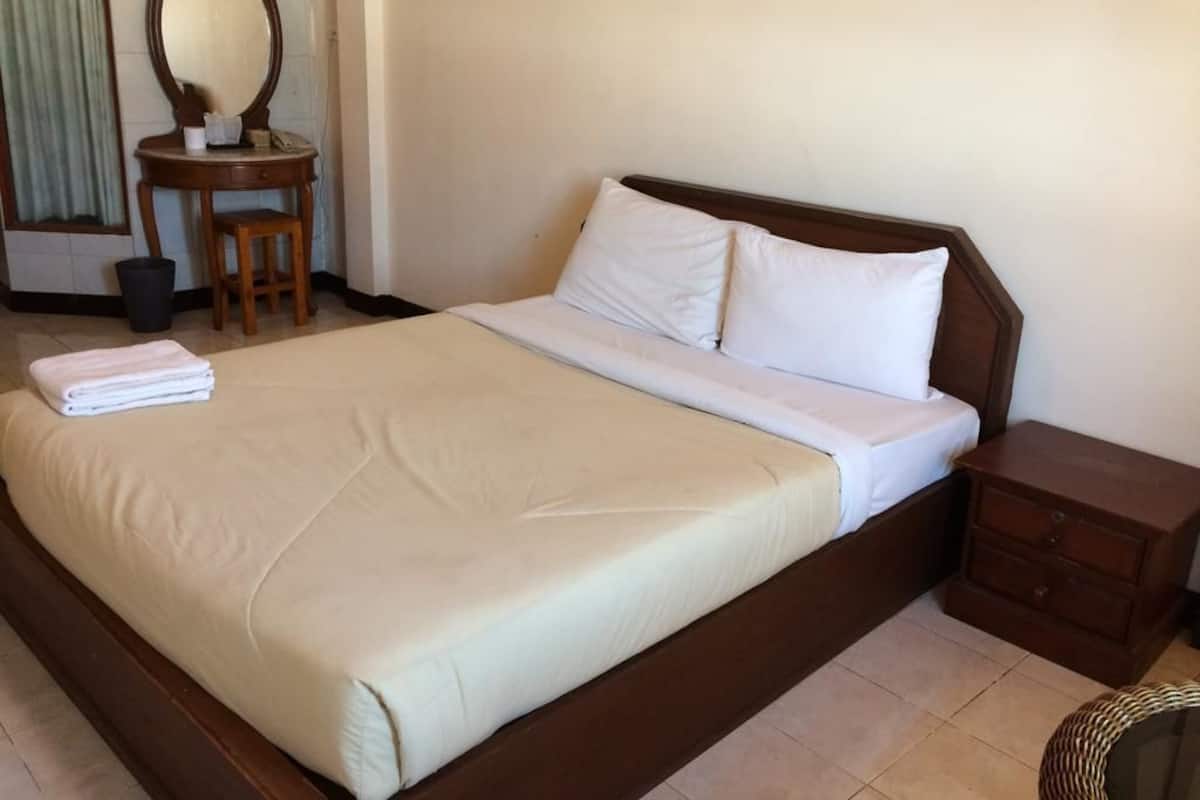 A neatly made bed with white linens, a wooden nightstand with a drawer, and a small round table with a mirror and a telephone.