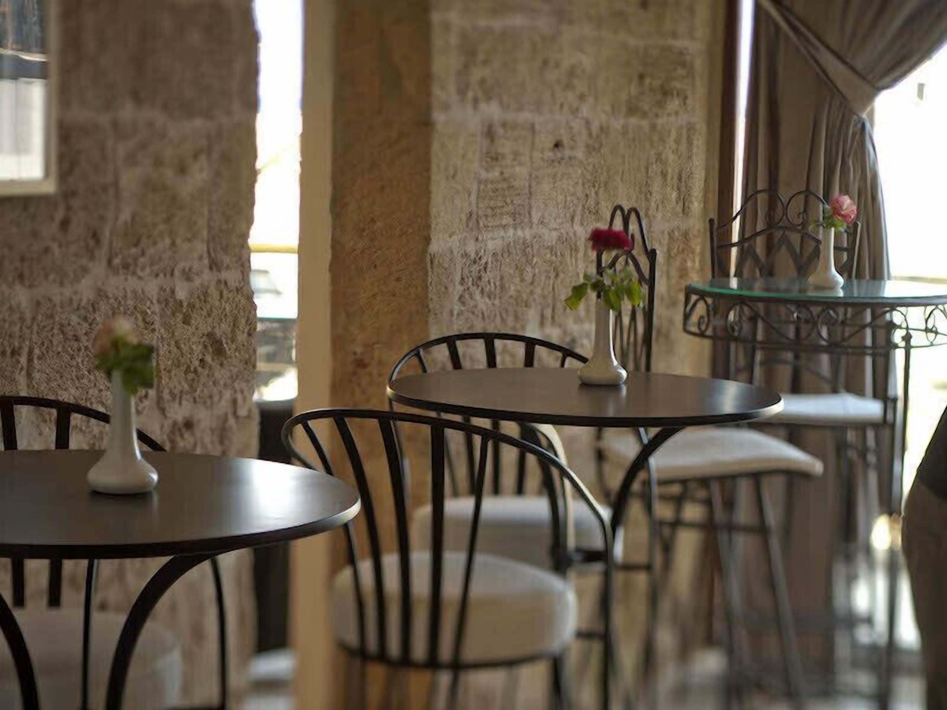 Un café aux murs de pierre, aux tables rondes et aux chaises en métal.