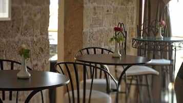 Un café aux murs de pierre, aux tables rondes et aux chaises en métal.