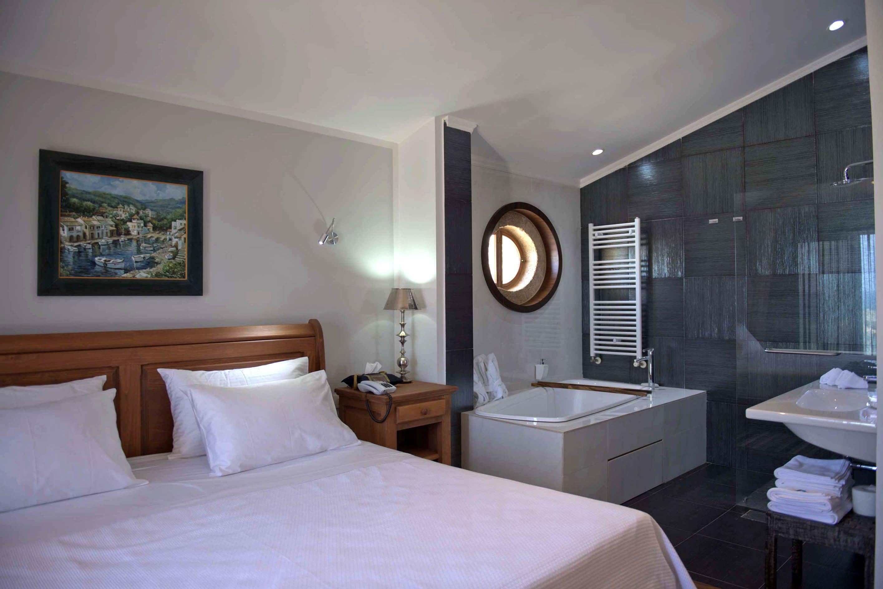 Une chambre d’hôtel comprenant un lit, une table de chevet, une lampe, un tableau, une baignoire, une douche et un lavabo.