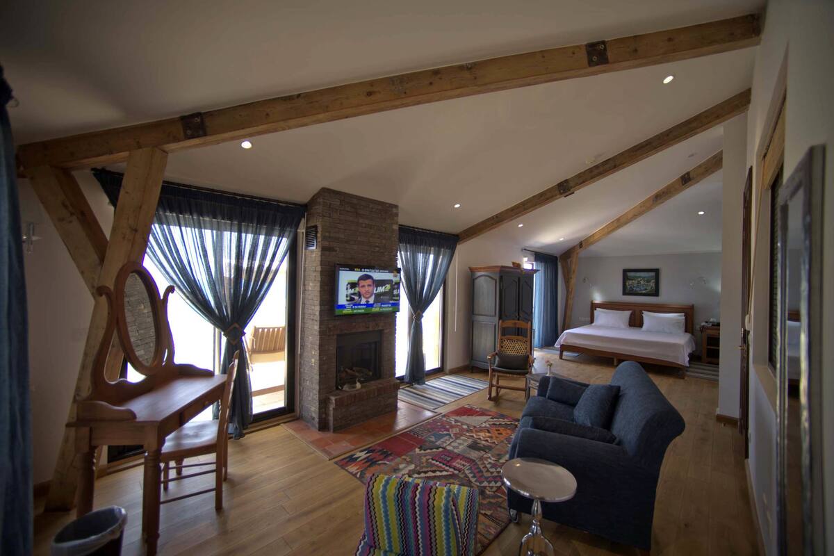 A spacious living room with a fireplace, a television, a sofa, and a bed in the background.
