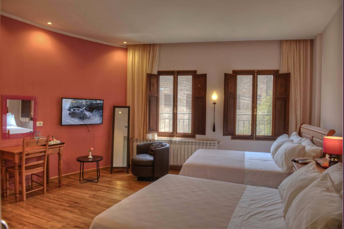 A hotel room with two beds, a desk, a chair, a TV, and a window with curtains.