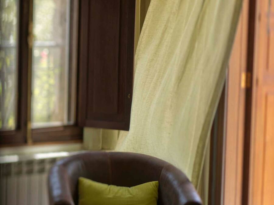 Una habitación con una cama, un sillón de cuero marrón con un cojín verde y una ventana con cortinas.