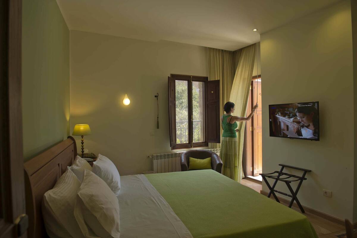 A hotel room with a bed, a TV, a window with curtains, and a chair.