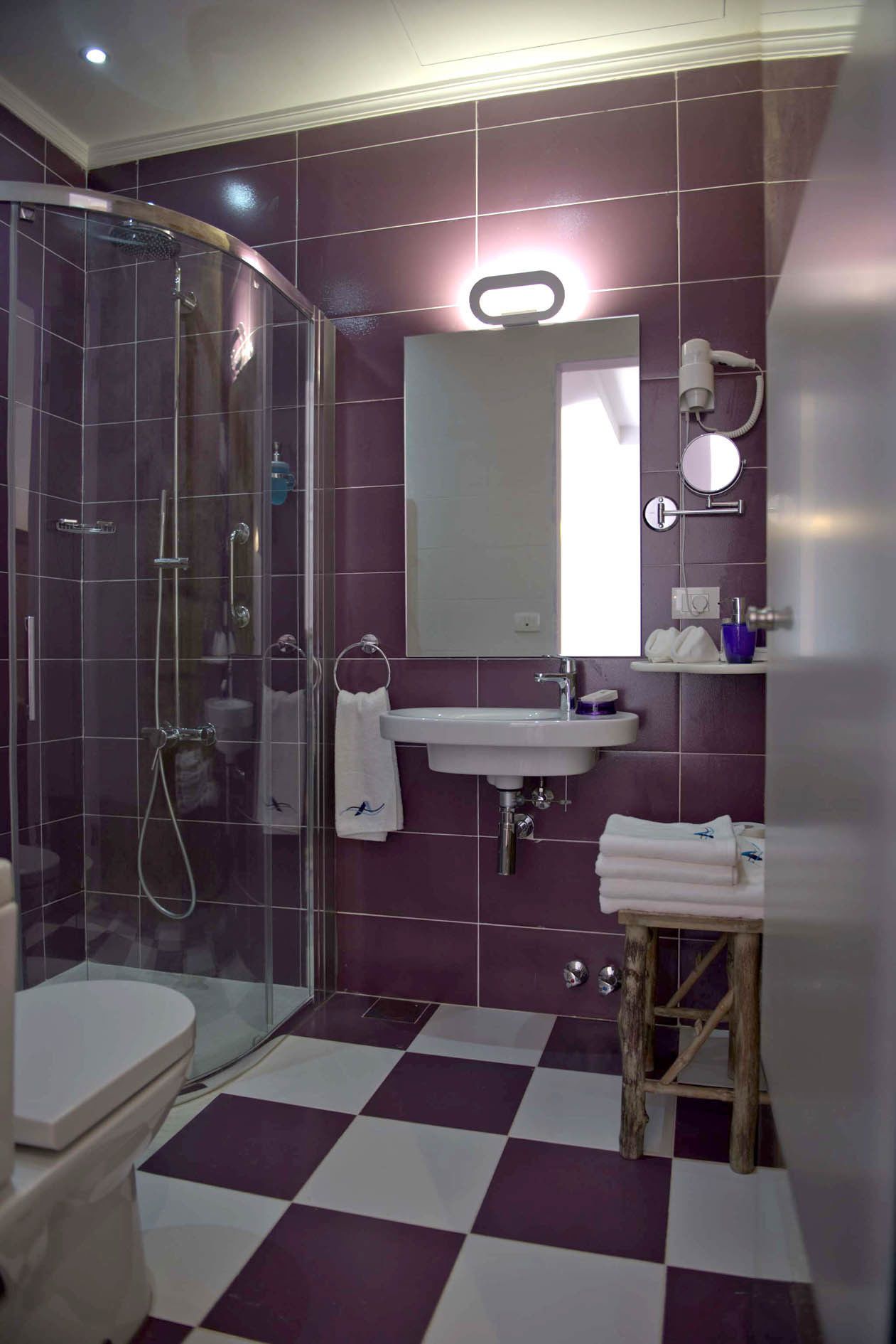 A bathroom with a glass-enclosed shower, a white sink, a mirror, and a wooden stool.