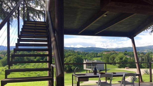 A wooden deck with a table and chairs, overlooking a scenic landscape with hills and trees. - Villa San Biagio (Colceresa)
