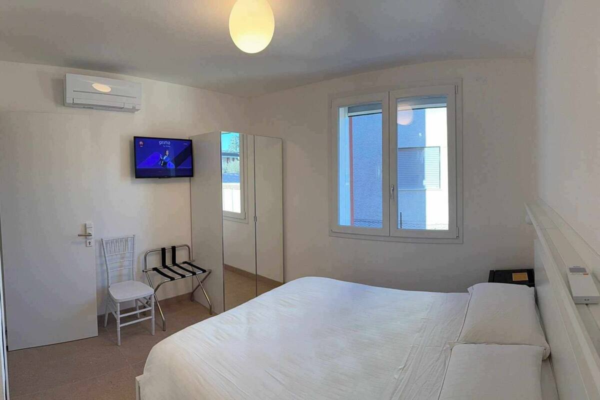 A bedroom with a bed, a television, a window, and a chair.