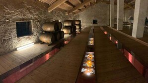 A cellar with wooden barrels and a long table with bottles. - Villa San Biagio (Colceresa)