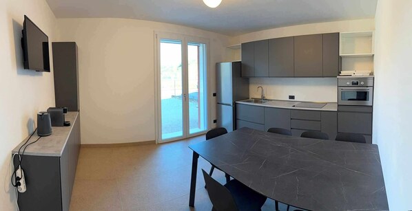 A modern kitchen with a large island, built-in appliances, and a sliding glass door leading to a balcony. - Villa San Biagio (Colceresa)