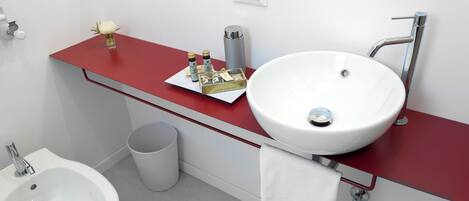 A bathroom with a white sink, a bidet, a red vanity, and a white towel hanging on the wall.
