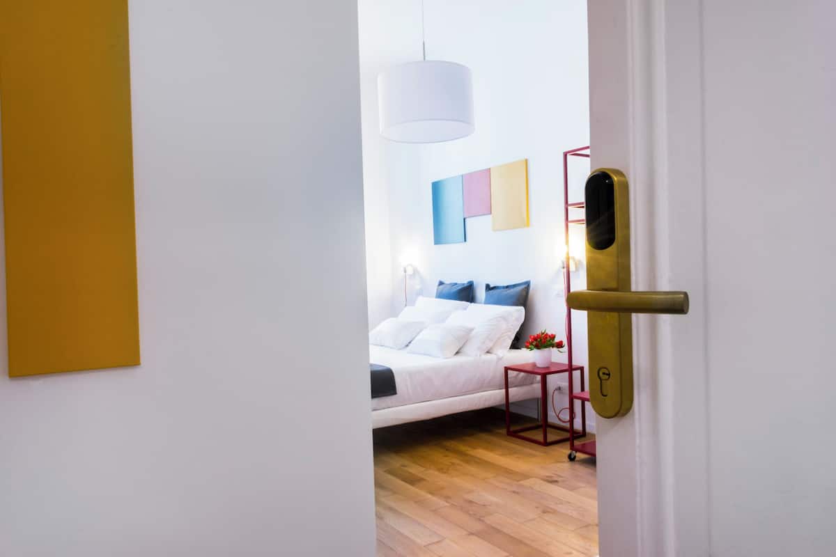 A bedroom with a bed, a bedside table, a hanging light fixture, and a door with a modern handle.