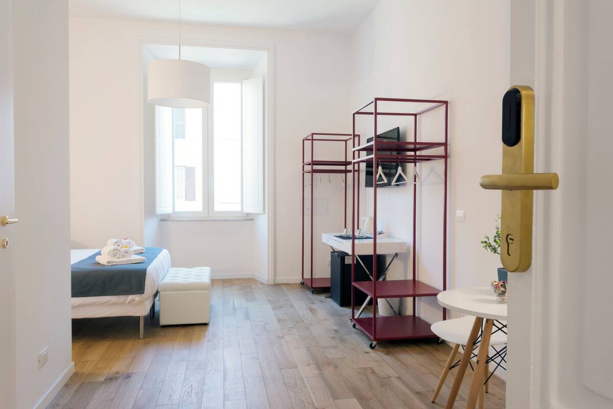 A hotel room with a bed, a desk, a chair, a window, and a wardrobe.