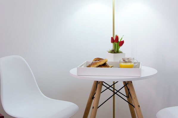 A white table with a tray containing a pastry, a glass of orange juice, and a small potted plant with red tulips. - Suite Cardinale (Rome)