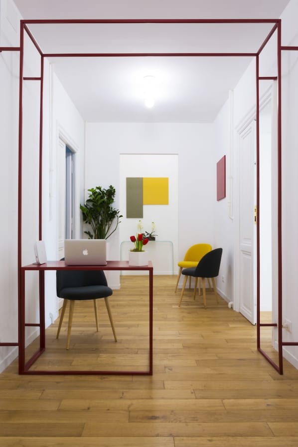 Ein modernes Zimmer mit Holzboden, Schreibtisch mit Laptop, Stuhl, Topfpflanze und gelber Sitzgelegenheit.