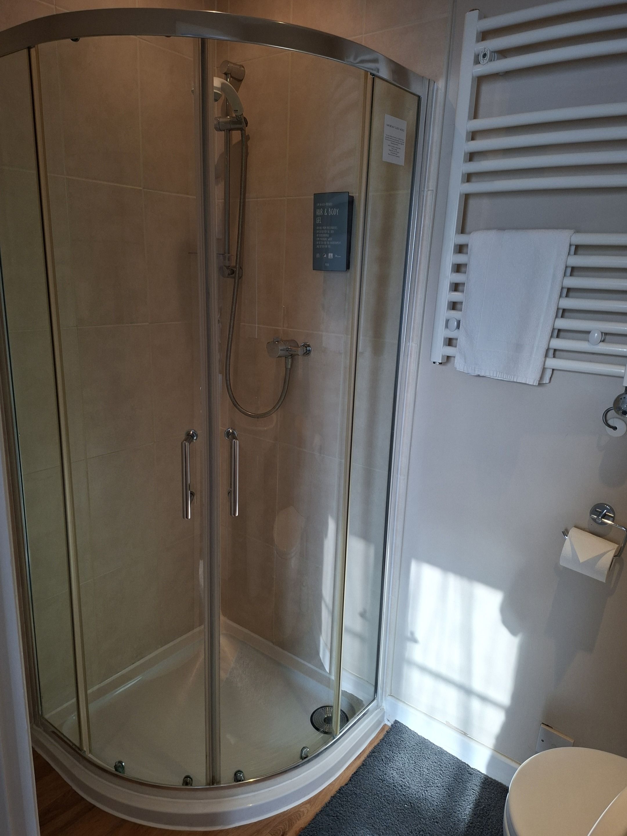 Cabina de ducha con paredes de vidrio, cabezal de ducha de mano y toallero en la pared.