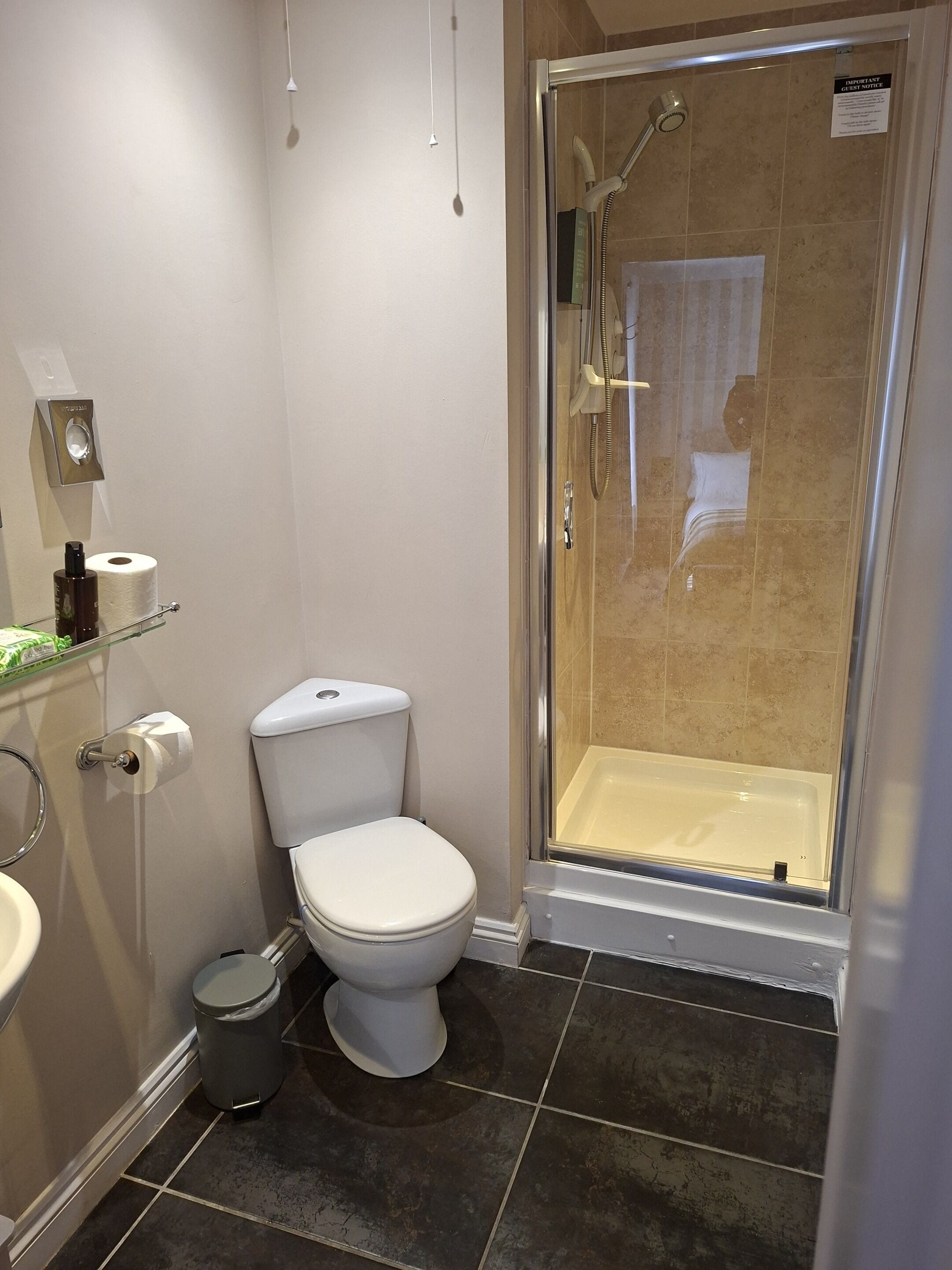Un baño con inodoro, un bote de basura, cabina de ducha y lavamanos.