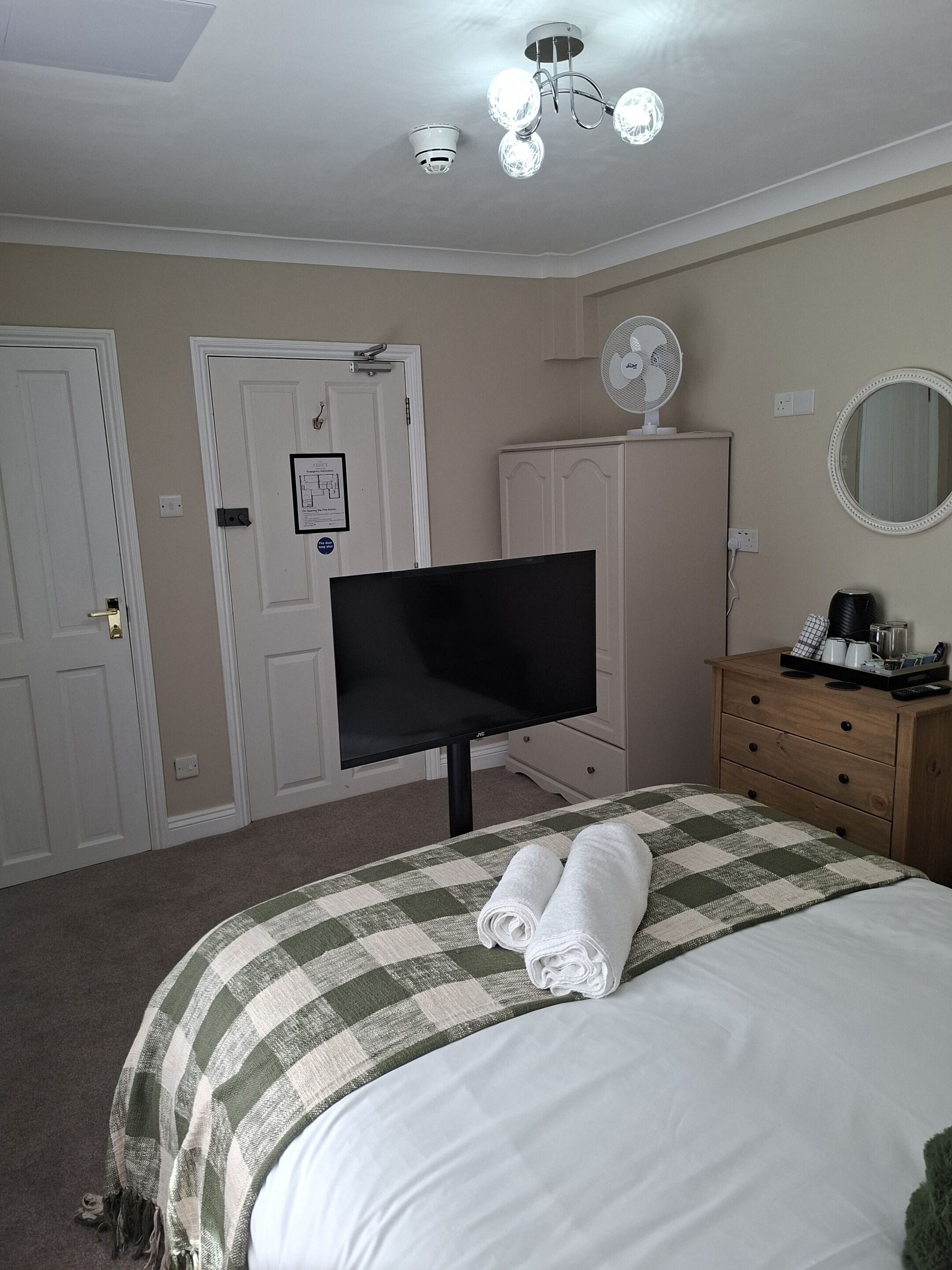A hotel room with a bed, a television, a dresser, a mirror, and a ceiling fan.