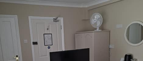 Habitación de hotel con cama, televisión, cómoda, espejo y ventilador de techo.