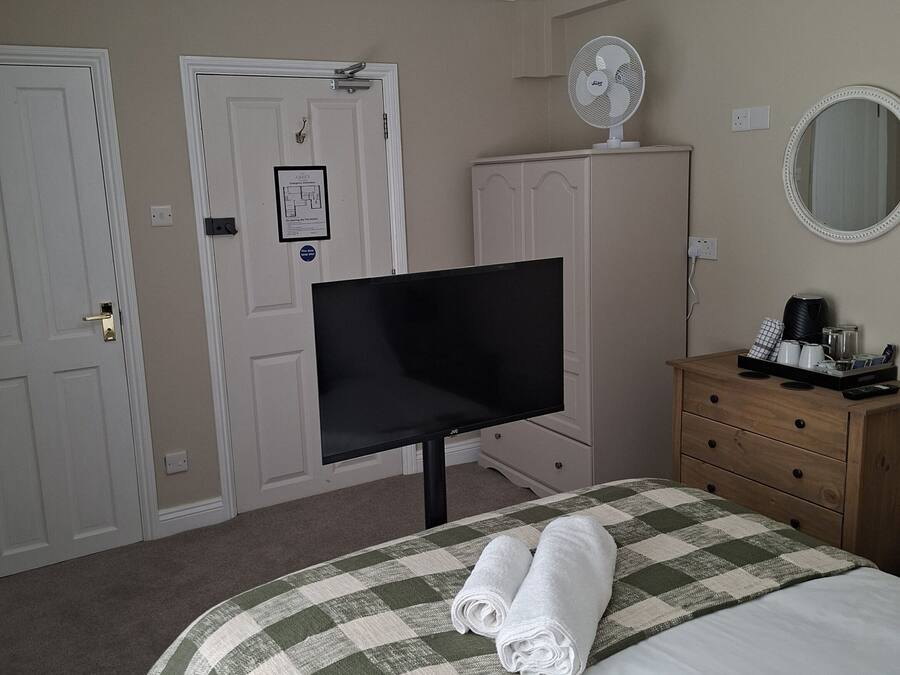 A hotel room with a bed, a television, a dresser, a mirror, and a ceiling fan.