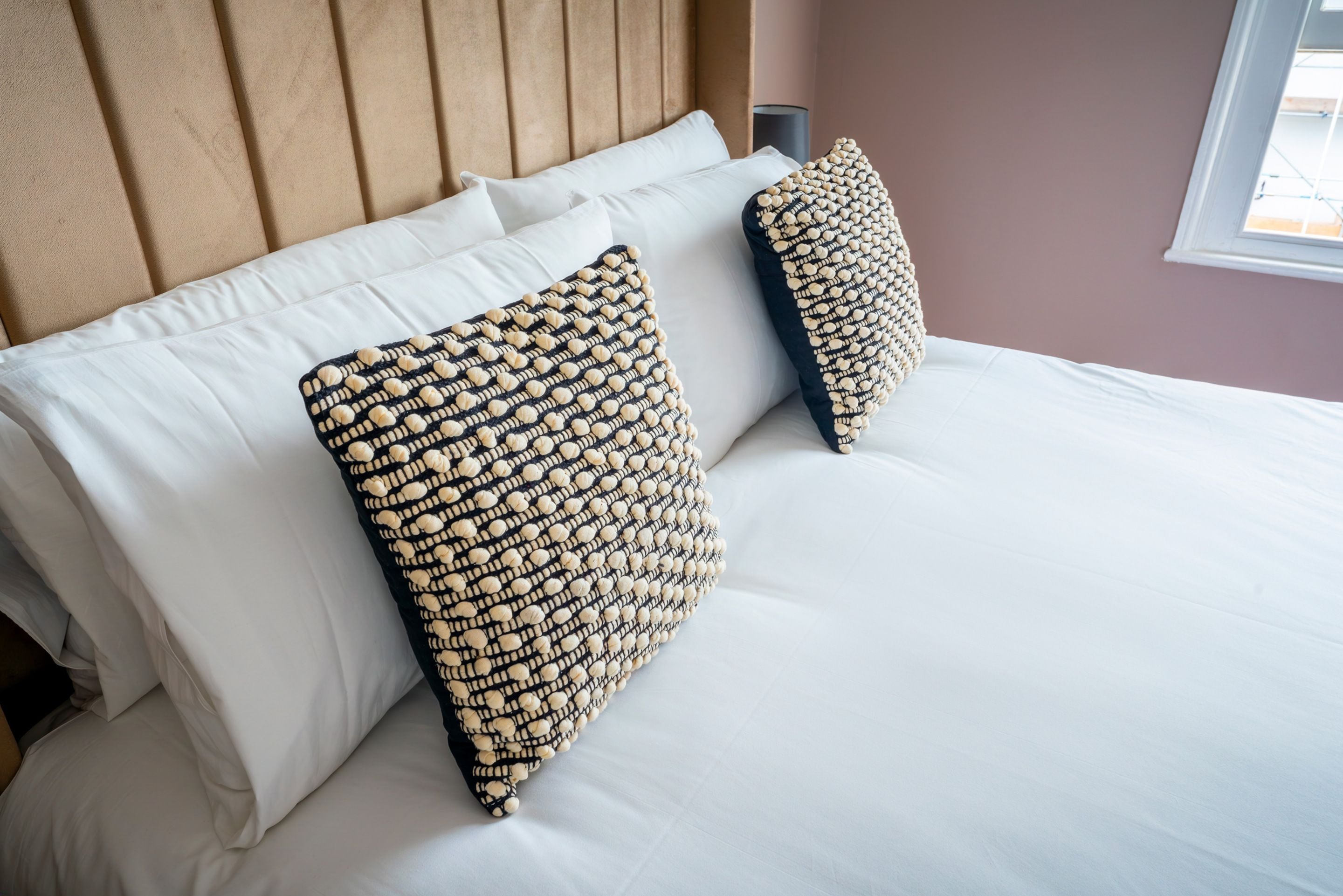 Un lit avec du linge de lit blanc et deux coussins décoratifs à motifs texturés.