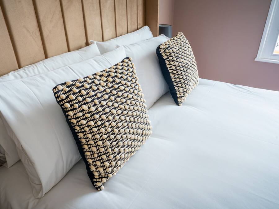 Una cama con sábanas blancas y dos almohadas decorativas con textura.