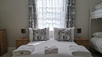 A neatly made bed with white linens, two bedside tables with lamps, and patterned curtains.