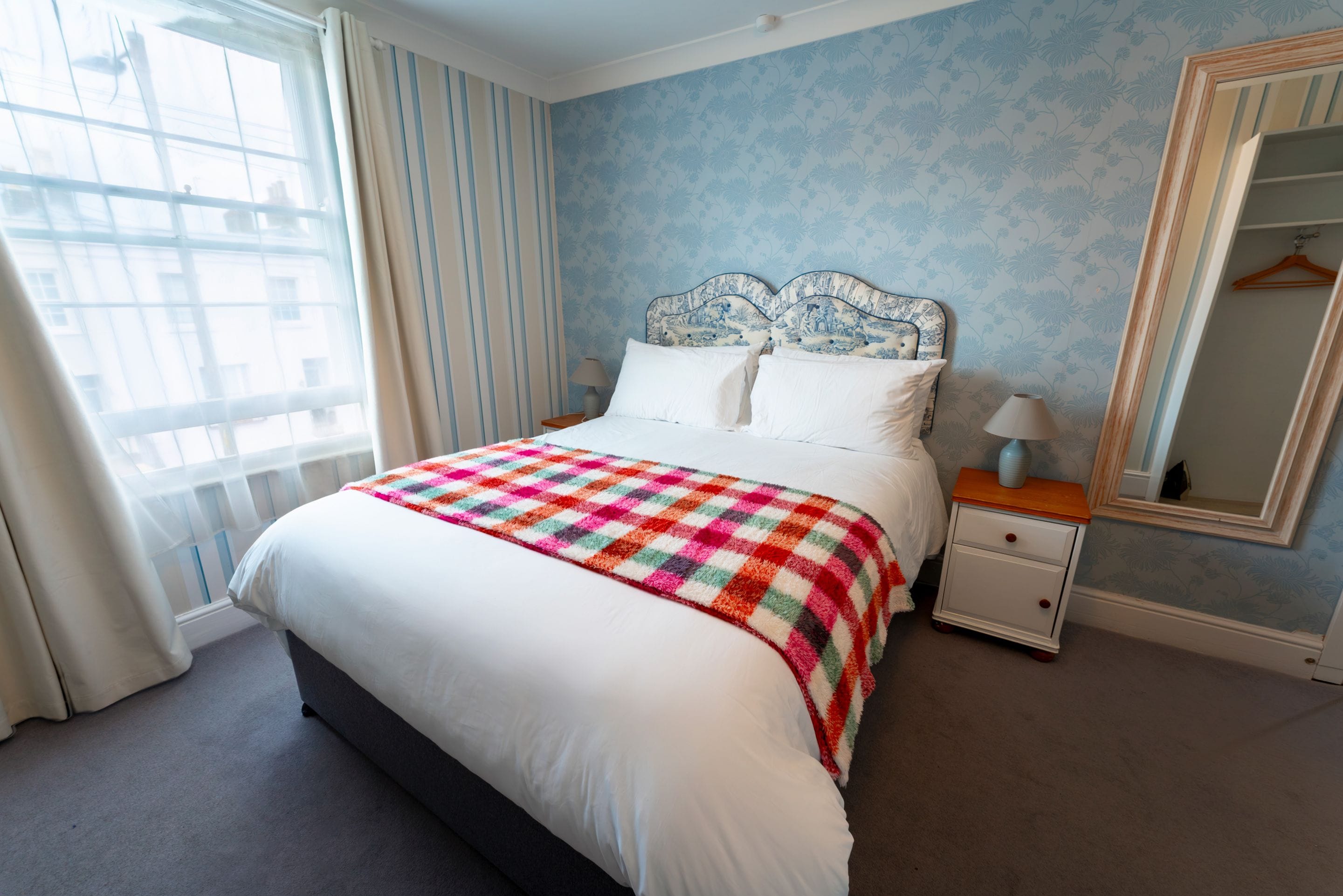 Une chambre d’hôtel avec un lit, une table de chevet, un miroir et une fenêtre avec des rideaux.