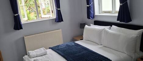 Une chambre à coucher avec un lit, un radiateur, une fenêtre avec des rideaux et une table de chevet avec une lampe.