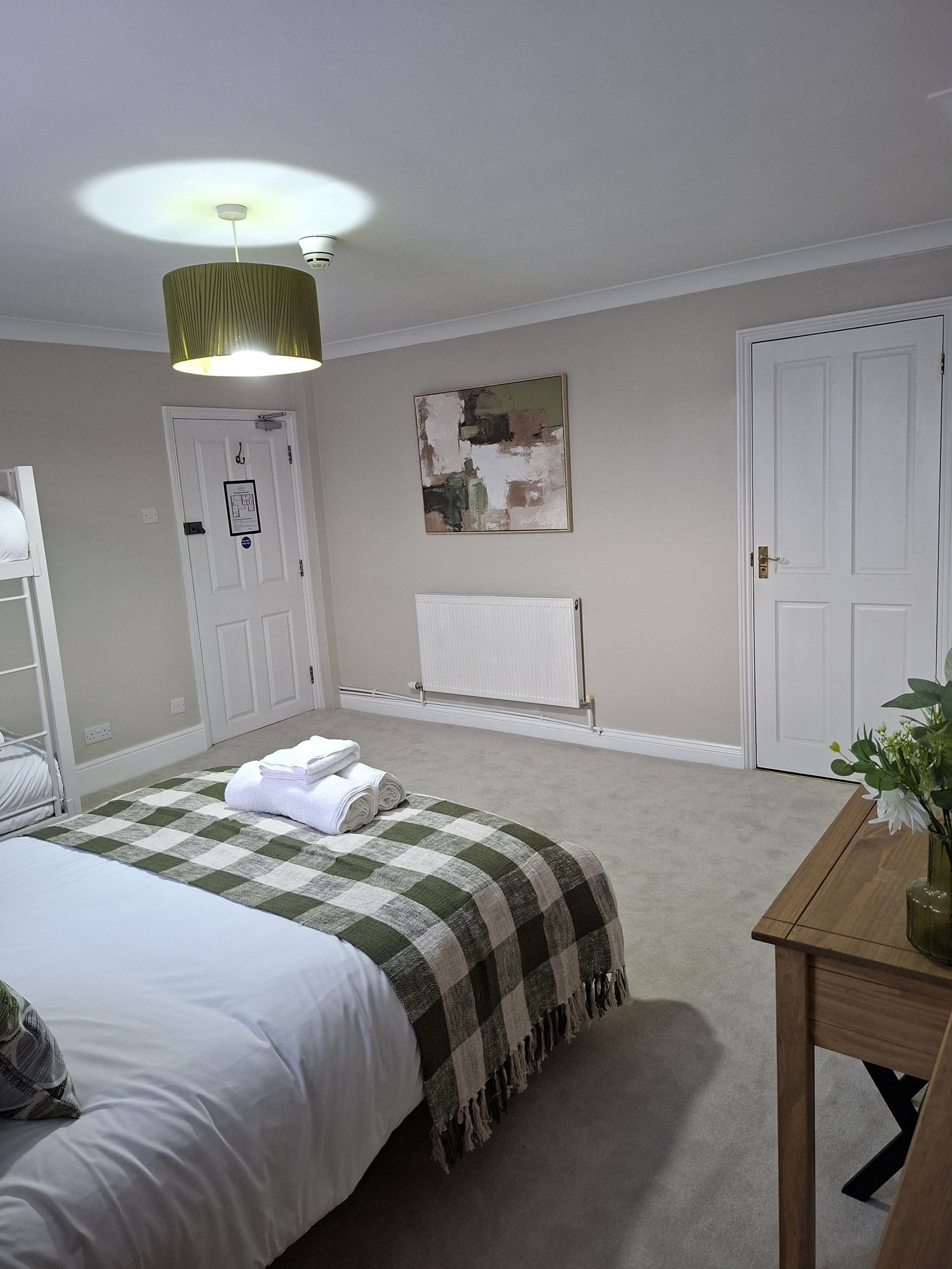 A bedroom with a bed, a bedside table with a vase, a radiator, and a door.