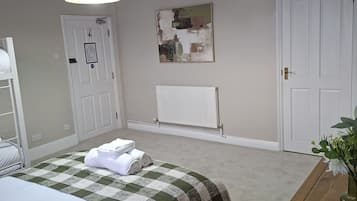 A bedroom with a bed, a bedside table with a vase, a radiator, and a door.
